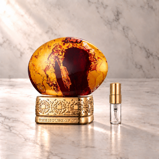 The House of Oud Almond Harmony Eau de Parfum mit 3-ml-Duftprobe aus Glas mit Goldkappe auf hellem Marmor